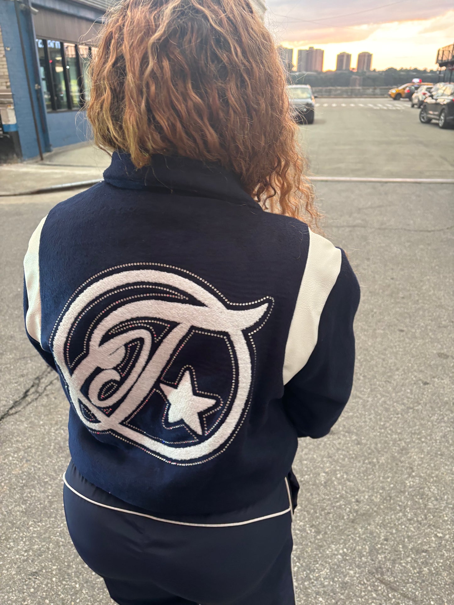 Person wearing a navy blue jacket with a logo on the back, standing outdoors.