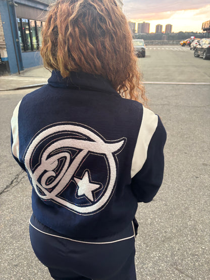 Person wearing a navy blue jacket with a logo on the back, standing outdoors.